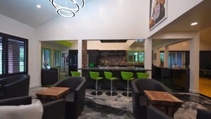 Un interior moderno con una zona de bar, taburetes verdes y una cocina al fondo.