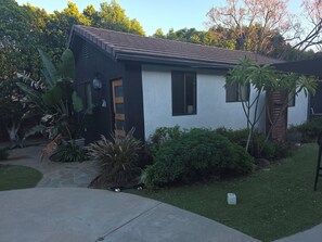 A single-story house with a dark exterior, a tiled roof, and a small front yard with various plants. - Spacious private Oasis (Los Angeles)