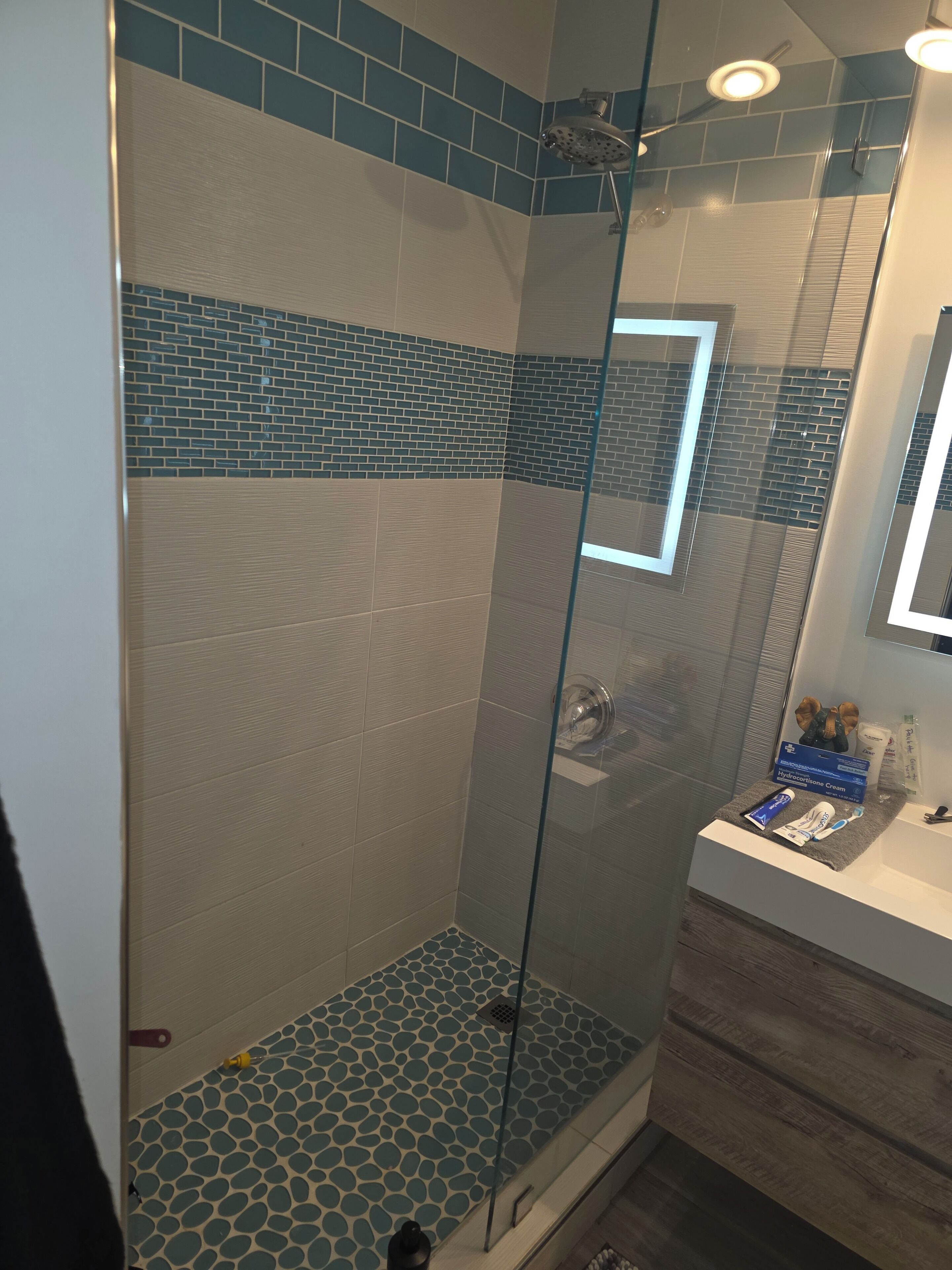 A shower with a glass door, a tiled floor, and a vanity with toiletries.
