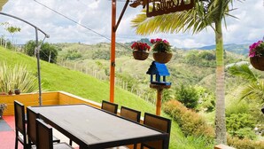 A patio with a table and chairs, overlooking a hilly landscape with greenery and a clear sky. - Nomad Nest Near Guatapé Jacuzzi Turkish Wifi-full (El Peñol)