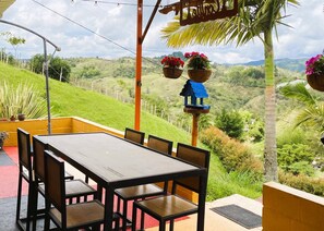 A patio with a table and chairs, overlooking a hilly landscape with greenery and a clear sky. - Nomad Nest Near Guatapé Jacuzzi Turkish Wifi-full (El Peñol)