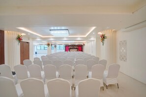 A conference room with rows of white chairs, a stage with floral decorations, and a modern ceiling design. - Deluxe Aarunya Residency And Banquets (Patna)