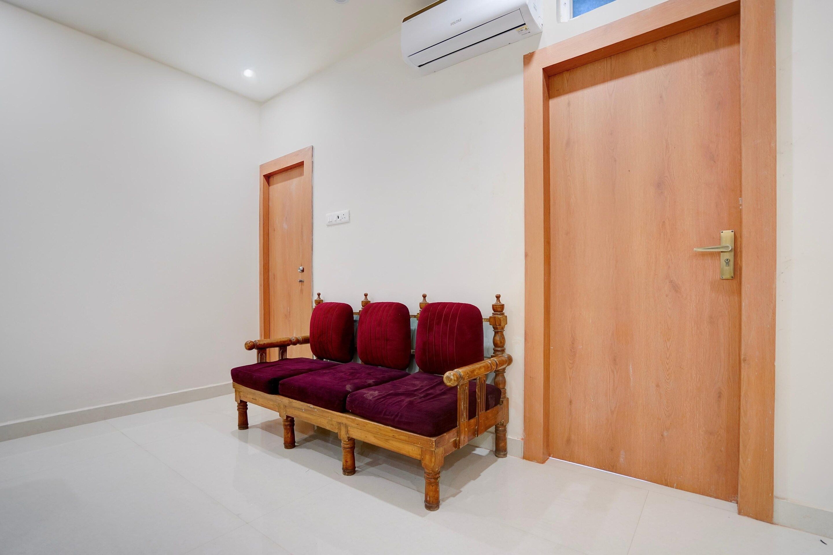 Una habitación con un banco de madera con cojines rojos, dos puertas de madera y un equipo de aire acondicionado en la pared.