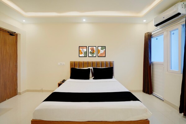 A hotel room with a bed, a bedside table, a phone, and a window with curtains.