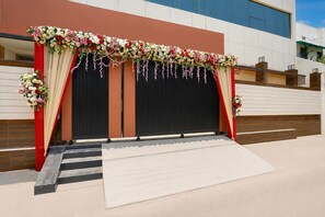 Un escenario con un telón de fondo rojo y blanco, flanqueado por arreglos florales y una escalera que lleva a él.