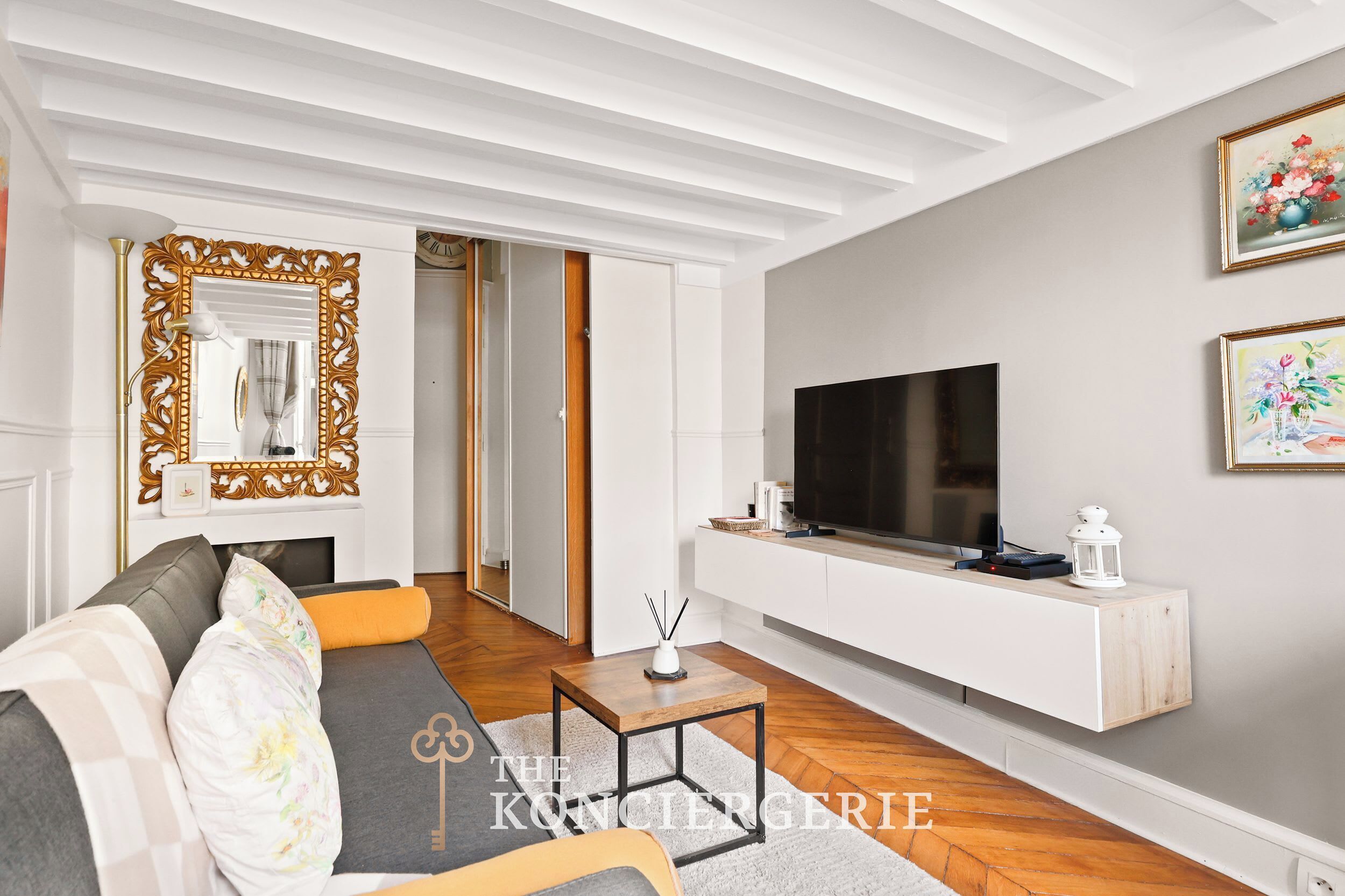 Un salon moderne doté d’un grand téléviseur à écran plat, d’un meuble de rangement blanc et d’un miroir décoratif orné d’un cadre travaillé.