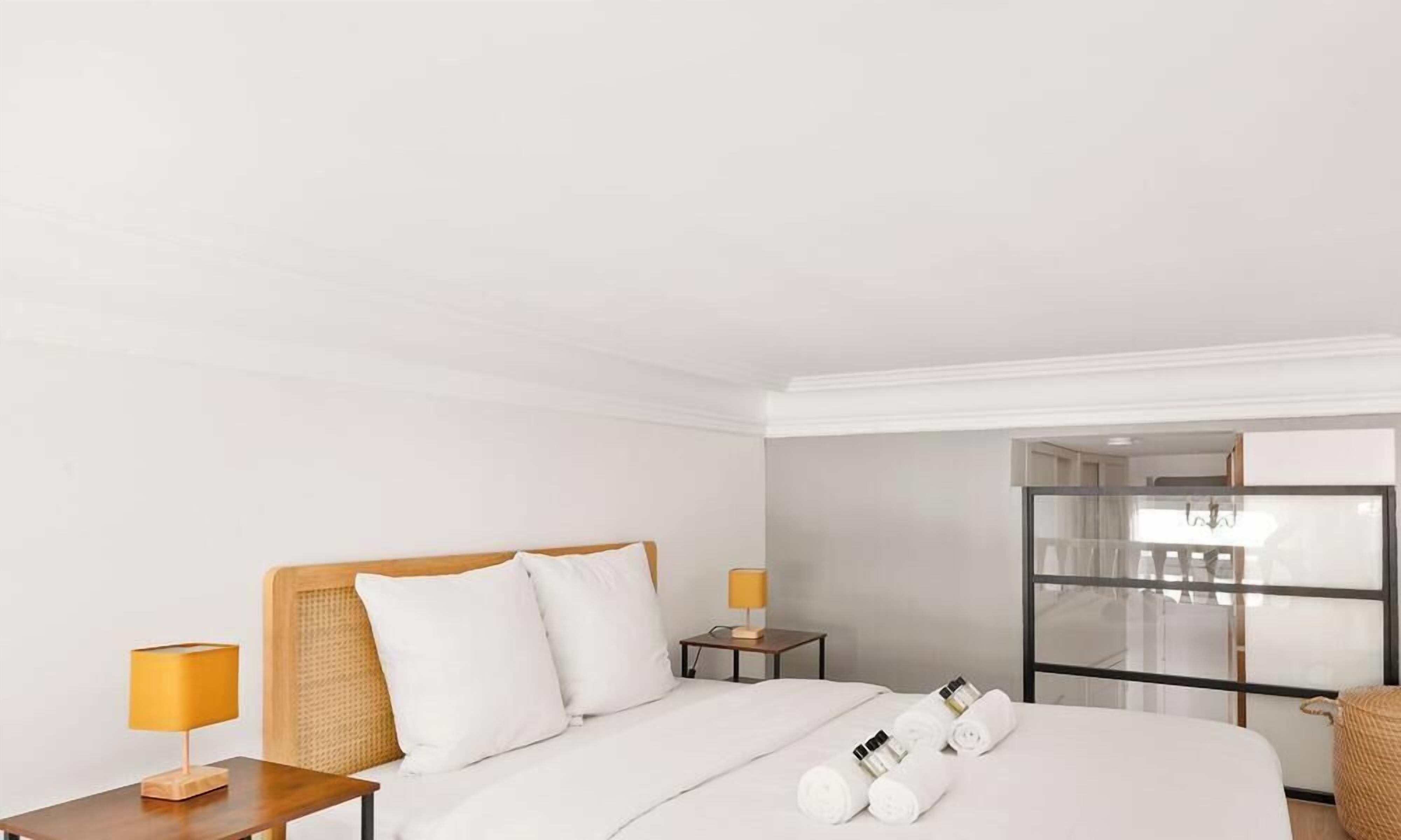 A hotel room with a bed, two bedside tables, a lamp, a woven basket, and a mirror.