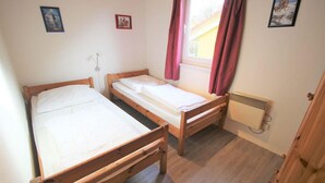A small room with two wooden beds, a radiator, and a window with curtains. - Skandinavischer Doppelbungalow mit Terrasse im Ferienpark Mirow (Mirow)