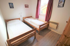 Ein kleines Zimmer mit zwei Holzbetten, einem Heizkörper und einem Fenster mit Vorhängen.
