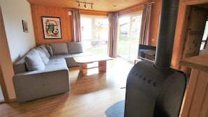 A modern living room with a sectional sofa, a wooden ceiling, and a large fireplace. - Skandinavischer Doppelbungalow mit Terrasse im Ferienpark Mirow (Mirow)