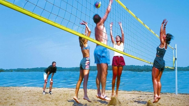 A group of people playing beach volleyball on a sandy beach with a clear blue sky and calm water in the background. - Skandinavischer Doppelbungalow mit Terrasse im Ferienpark Mirow (Mirow)