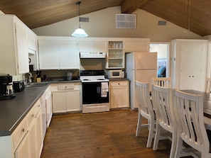 A kitchen with white cabinets, a stove, a microwave, and a refrigerator.