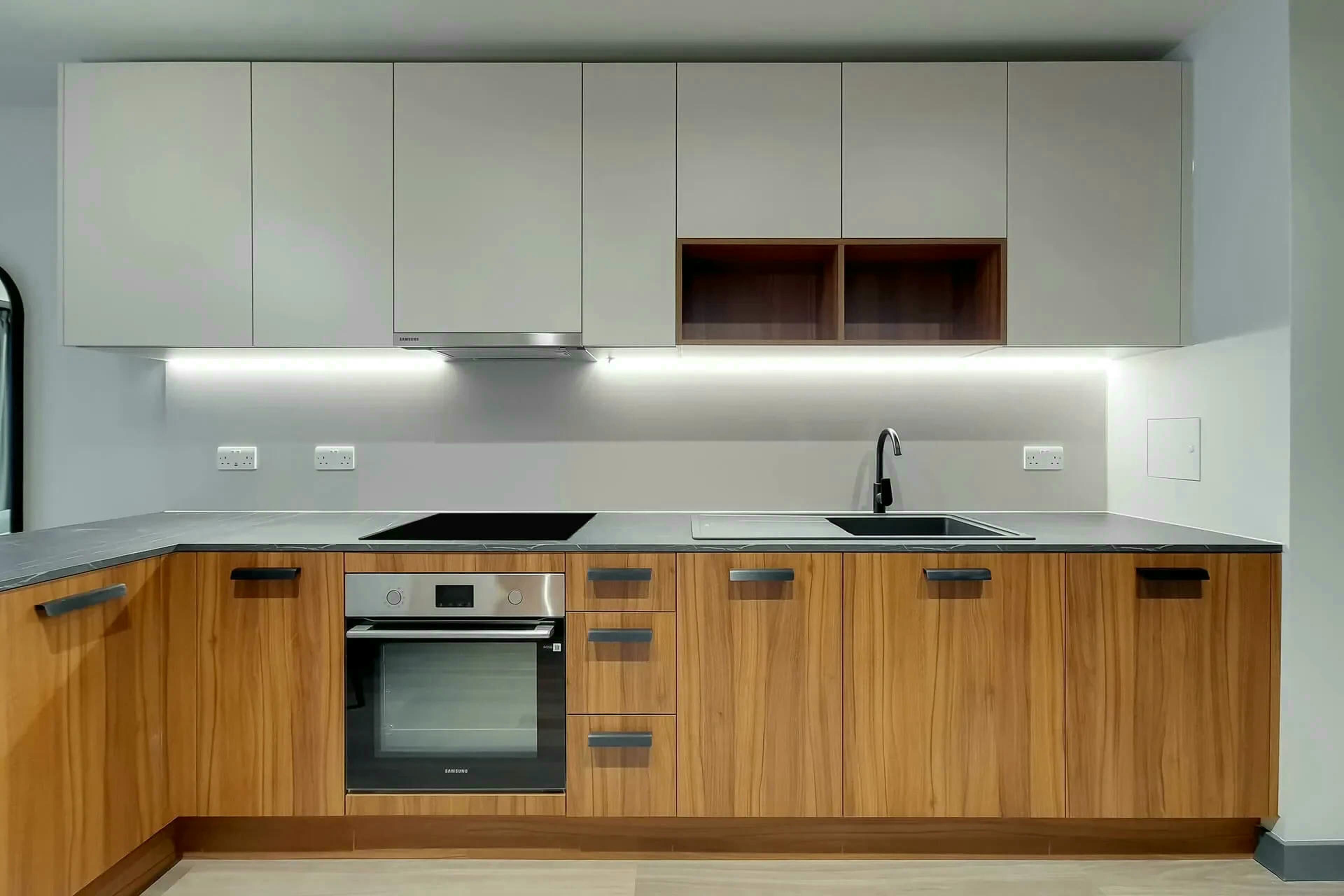 Eine moderne Küche mit Holzschränken, einem Edelstahlbackofen und einer eingebauten Mikrowelle.