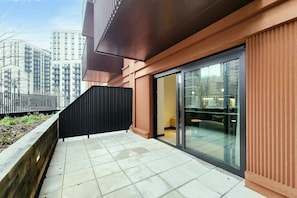 A modern building with a glass door entrance, a black fence, and a tiled patio area.