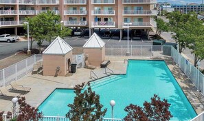 A rectangular swimming pool with a white fence, lounge chairs, and a small building with a white roof. - Lorelei II 405 - Your perfect Ocean City getaway! (Ocean City)