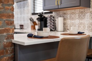 A kitchen with a brick wall, a white countertop, and a patterned backsplash.