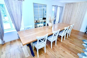A dining area with a wooden table and white chairs, a large window with curtains, and a view of the outdoors. - Domaine de L'Olymp (Cornant)