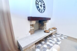 A fireplace with a stone base, a wooden mantel, and a clock above it. - Domaine de L'Olymp (Cornant)