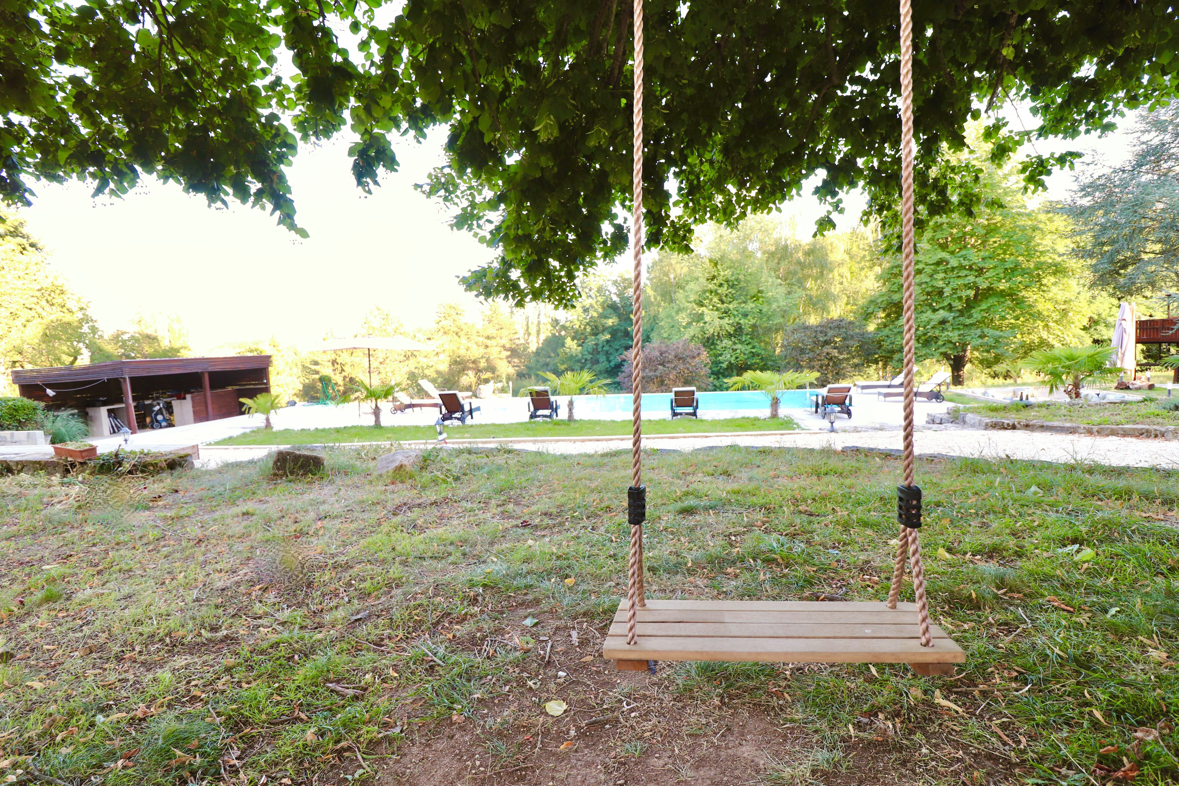 Ein hölzernes Schaukelgerüst in einem Park, im Hintergrund ein Schwimmbecken.