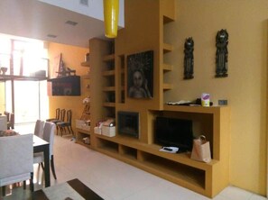 Un soggiorno con TV, scaffali e zona pranzo.