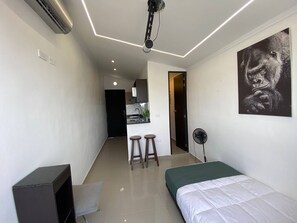 Ein modernes Hotelzimmer mit Bett, Schreibtisch, Stuhl, einer kleinen Küchenzeile und einem Deckenprojektor.