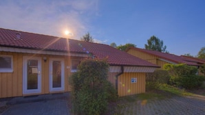 A building with a tiled roof, a paved driveway, and a small parking area. - Urlaub im Grunen - Doppelbungalow mit Terrasse im Ferienpark Mirow (Mirow)