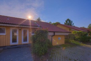 A building with a tiled roof, a paved driveway, and a small parking area. - Urlaub im Grunen - Doppelbungalow mit Terrasse im Ferienpark Mirow (Mirow)