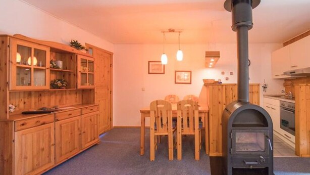 A cozy room with wooden cabinets, a dining table with chairs, a wood-burning stove, and pendant lighting. - Urlaub im Grunen - Doppelbungalow mit Terrasse im Ferienpark Mirow (Mirow)