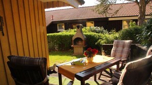 An outdoor patio with a wooden table, two chairs, and a pizza oven. - Urlaub im Grunen - Doppelbungalow mit Terrasse im Ferienpark Mirow (Mirow)