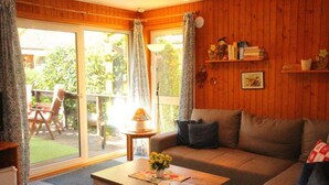 A cozy living room with a sofa, a coffee table, and a view of a garden through a sliding glass door. - Urlaub im Grunen - Doppelbungalow mit Terrasse im Ferienpark Mirow (Mirow)