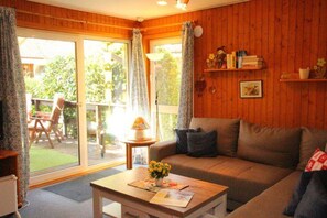 A cozy living room with a sofa, a coffee table, and a view of a garden through a sliding glass door. - Urlaub im Grunen - Doppelbungalow mit Terrasse im Ferienpark Mirow (Mirow)