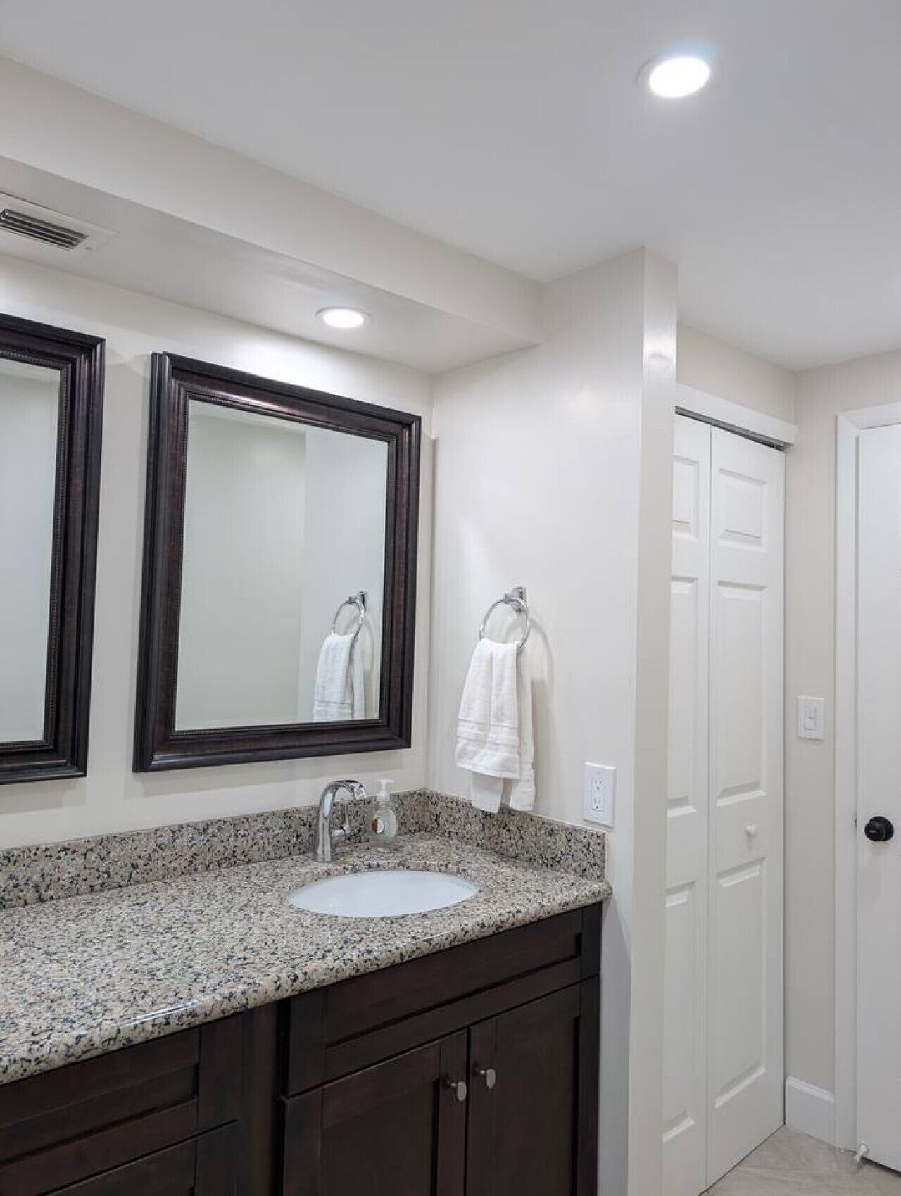 A bathroom with a granite countertop, a sink, two mirrors, a towel rack, and a white door.