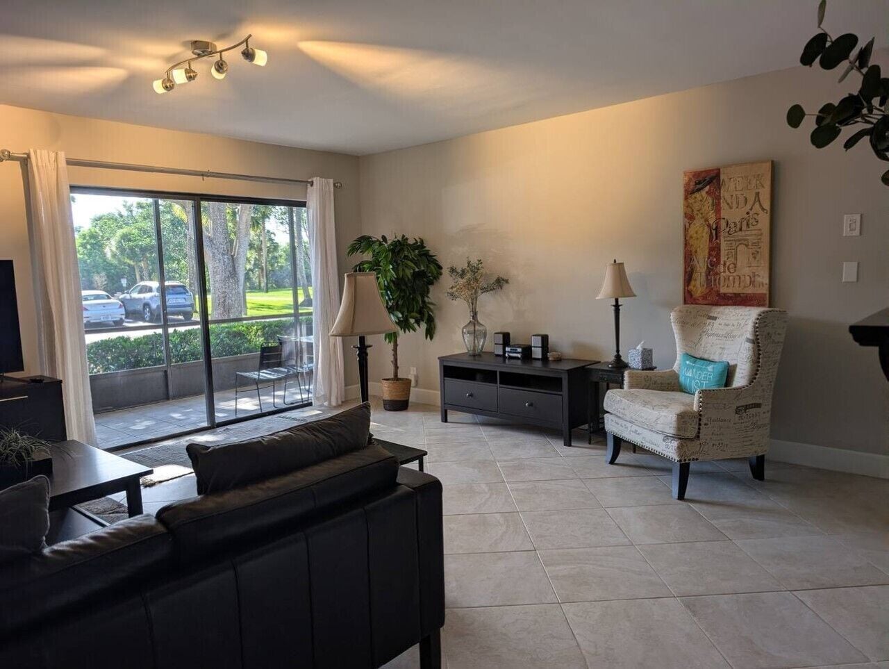 A modern living room with a sofa, armchair, and a small table. There is a large window with a view of the outside.