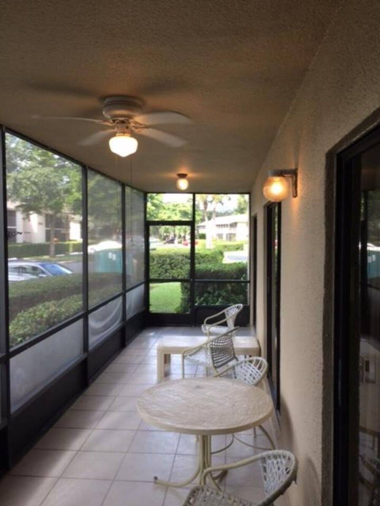 A covered balcony with a table and chairs, large windows, and a ceiling fan.