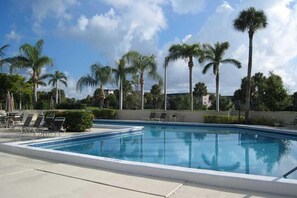 Ein Swimmingpool mit Liegestühlen, Palmen und blauem Himmel.