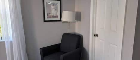 Une pièce avec un fauteuil noir, une porte blanche, un tableau encadré au mur et une lampe.