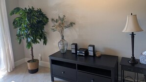 Ein Zimmer mit einem dunkelbraunen Konsolentisch, einer Topfpflanze, einer Blumenvase, einer Lampe und einem kleinen Lautsprecher.
