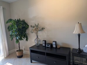 Ein Zimmer mit einem dunkelbraunen Konsolentisch, einer Topfpflanze, einer Blumenvase, einer Lampe und einem kleinen Lautsprecher.