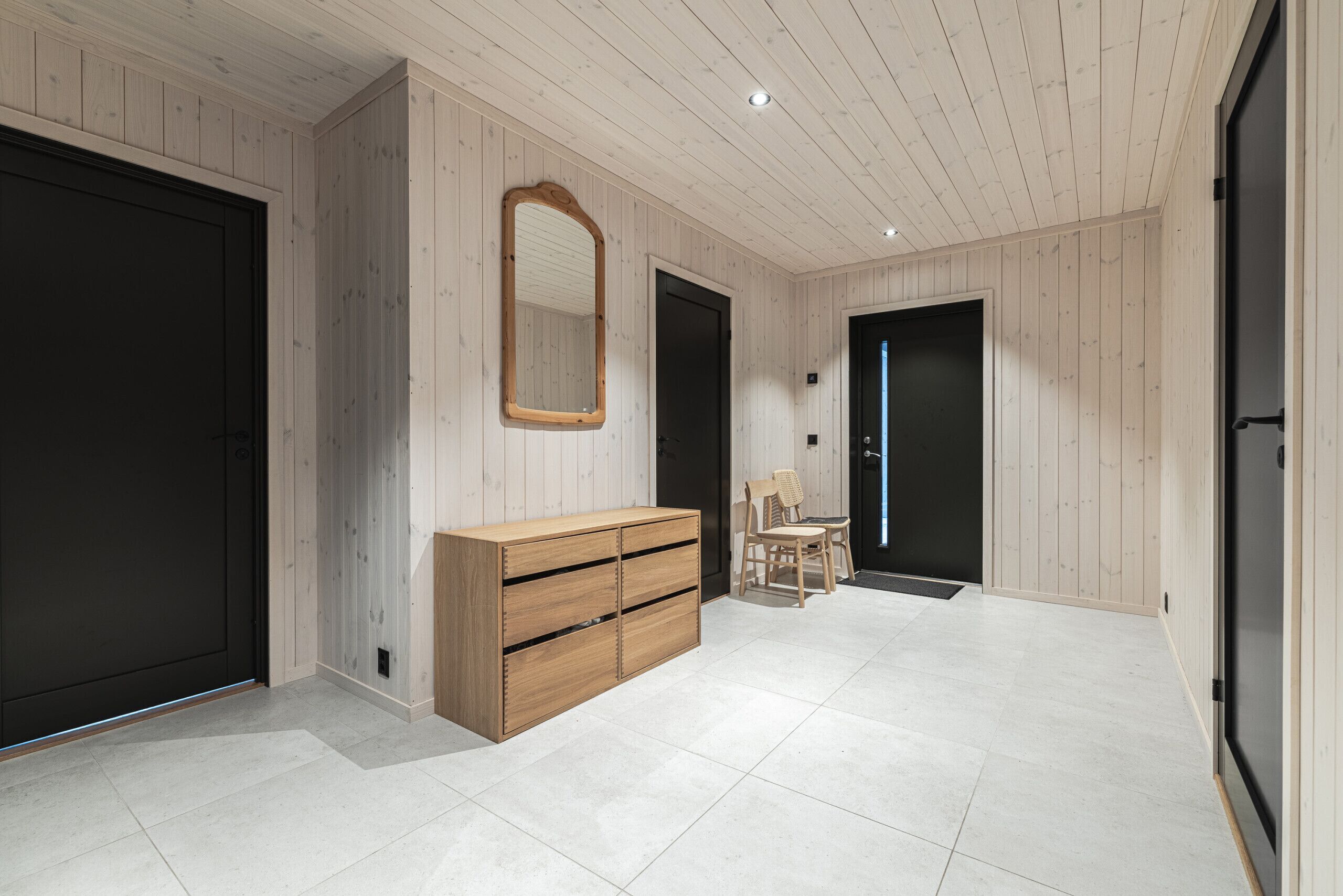 Ein modernes Interieur mit Holzwandverkleidung, einer Holzkommode, einem Spiegel und zwei Türen.