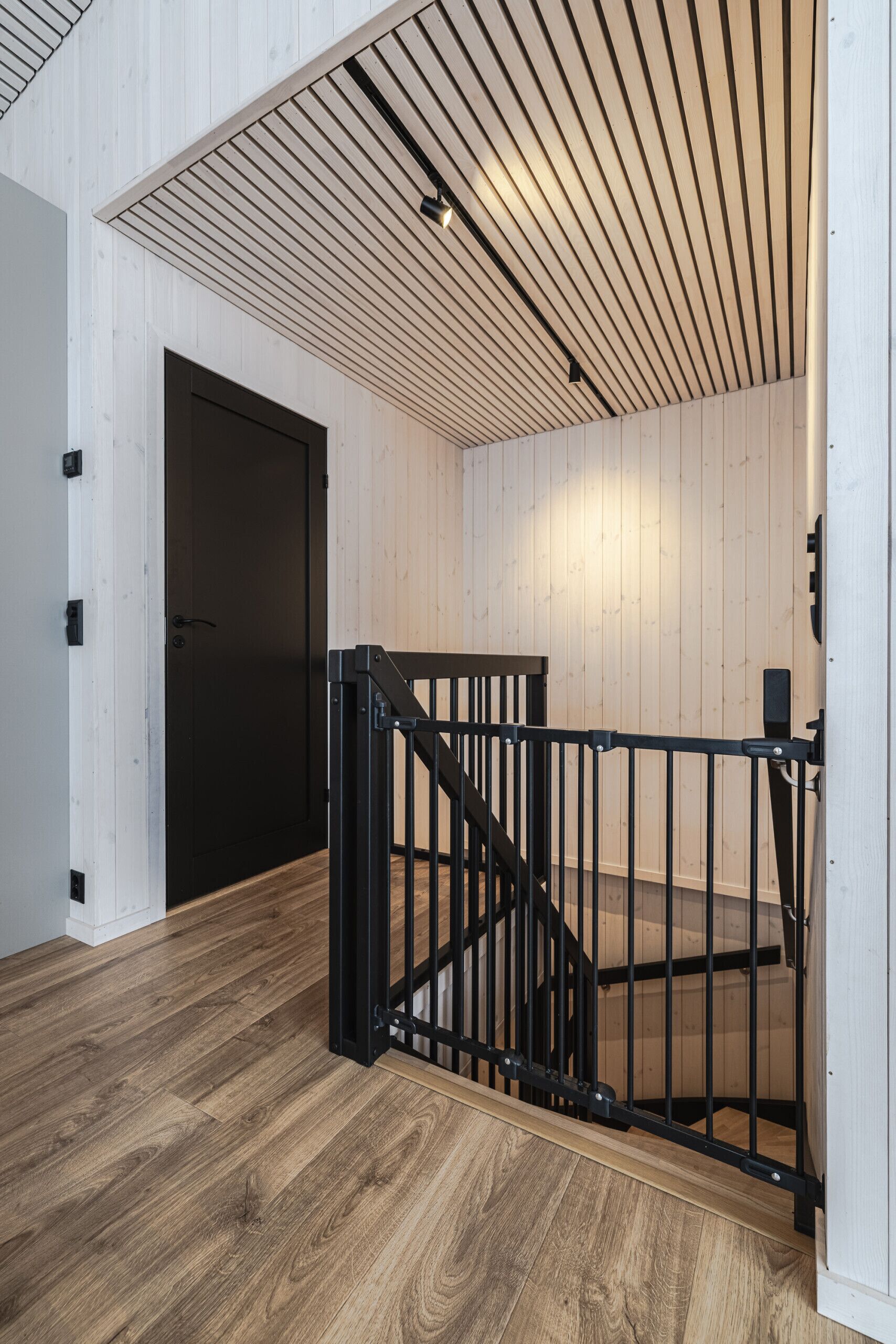 A modern interior with a wooden floor, a black door, and a staircase with a metal railing.