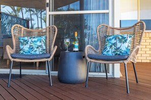 Two wicker chairs with blue cushions, a bottle of wine, and a glass on a table on a wooden deck. - Blue Waters- Riverview Escape for the whole family (Kalbarri)