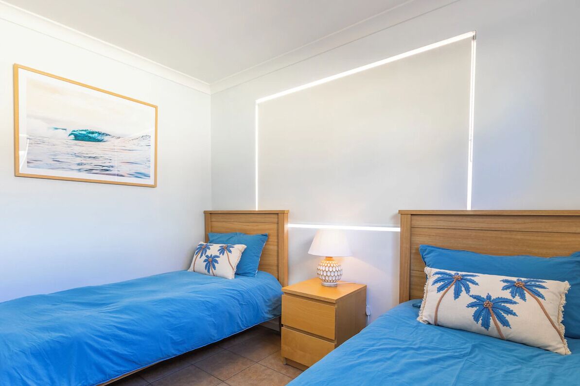 A bedroom with two beds, a nightstand, a wall-mounted lamp, and a framed picture.