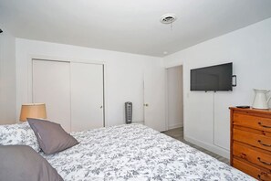 A bedroom with a bed, a dresser, a heater, a TV, and a door. - Cozy house with heated pool near the beach (Lighthouse Point)