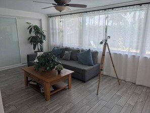 Ein Wohnzimmer mit einer Couch, einem Couchtisch mit Pflanze, einem Teleskop und einem Deckenventilator.