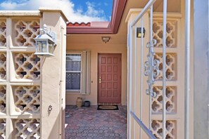 A house entrance with a red door, a window with a patterned curtain, and a decorative metal gate. - Cozy house with heated pool near the beach (Lighthouse Point)