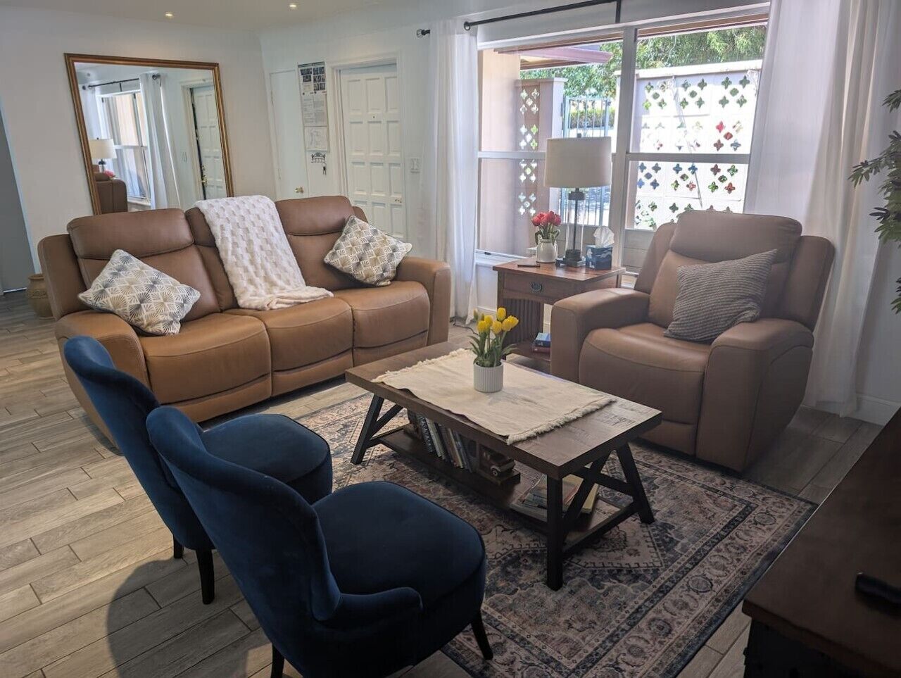 A living room with a brown sofa, a blue armchair, a wooden coffee table, and a patterned rug.