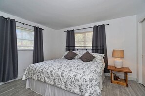 Une chambre à coucher avec un lit, des rideaux, une table de chevet avec une lampe et une petite étagère avec des livres et un jouet.