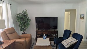 A living room with a sofa, a chair, a television, and a plant.