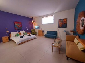 Un dormitorio con cama, sofá azul, una mesita de centro, televisor y obras de arte en las paredes.