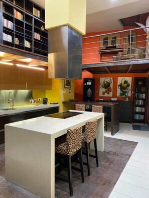 Una cucina moderna con isola centrale, sgabelli da bar e una libreria.